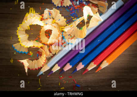 Colored pencils placed in row with pencils peeled of various colors in the background, such as blue, purple, pink, red, orange and silver. Arranged on Stock Photo