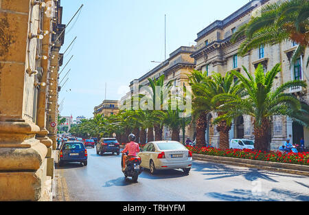 FLORIANA, MALTA - JUNE 19, 2018: The long traffic jam in St Anne avenue, decorated with line of palm trees and bright red flowers, on June 19 in Flori Stock Photo