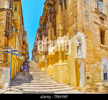 VALLETTA, MALTA - JUNE 19, 2018: The medieval St John street with staircase, running to the hilltop, old stone buildings and wall statue of St Anthony Stock Photo