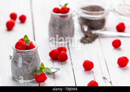 Closeup of served glass jars filled with sweet pudding of chia seeds and garnished with fresh raspberry and mint Stock Photo