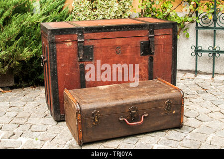 Old retro wooden chest and vintage grunge suitcase isolated on stone paved house backyard Stock Photo