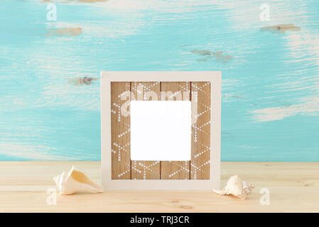 blank white photo frame and sea shells over wooden table and pastel blue background. Ready for photography montage Stock Photo