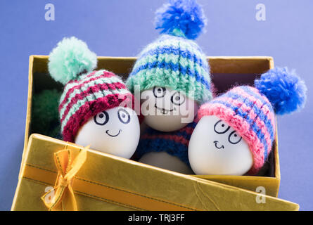 Beautiful Easter eggs with cheerful faces lie in a yellow gift box with small caps. Easter Stock Photo