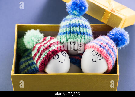 Beautiful Easter eggs with cheerful faces lie in a yellow gift box with small caps. Easter Stock Photo