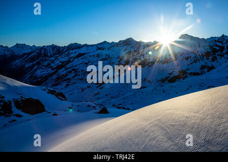 New snow on a bright sunny morning in the Talkeetna Mountains near the Snowbird Glacier. Sunrise peeking over the high mountain ridgeline. Stock Photo