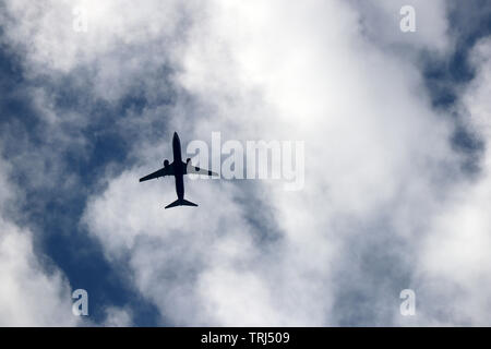 Airplane flying in the sky on background of clouds. Silhouette of a commercial plane, turbulence concept Stock Photo