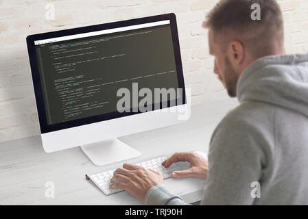 Man coding app on a computer. Close-up scene. Clean office desk with brick wall in background. Stock Photo