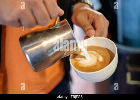 Barista pouring milk on coffee cup making heart shape Stock Photo