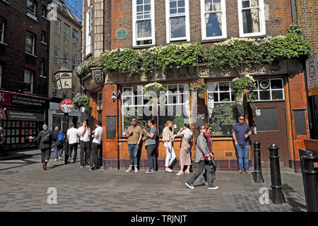 Crowd of people standing drinking pints of beer outside the The Blue Posts pub in Berwick Street, Soho in London England UK  KATHY DEWITT Stock Photo