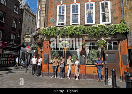 Crowd of people standing drinking pints of beer outside the The Blue Posts pub in Berwick Street, Soho in London England UK  KATHY DEWITT Stock Photo