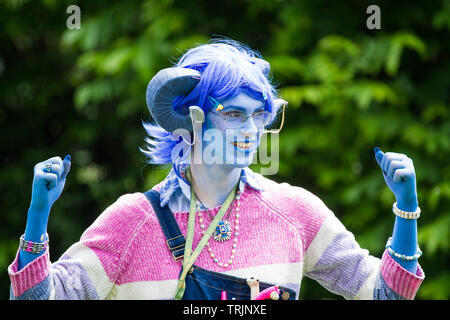 NEC, BIRMINGHAM, UK - JUNE 1, 2019. A male osplayer cross dressed as girl in a feminine colourful critters outfit with blue face at a comic con event Stock Photo