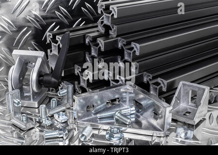 stack of black anodized aluminum extrusion bars, connector, joint, screw , slot nut and angle bracket on silver shiny diamond plate background. Constr Stock Photo