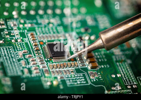 Soldering a micro chip processor with iron tool on a green circuit boad. Electroncs service technology and macro computer concept background. Stock Photo
