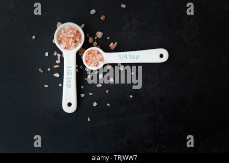 Pink Himalayan salt in measuring spoons on black background. Stock Photo