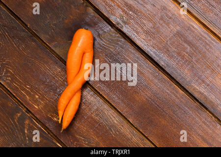 Ugly twisted carrot on wooden background. Image with copy space, top view. Stock Photo