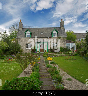 Picturesque stone cottage with pathway leading through colourful garden and lawns under blue sky in Scotland Stock Photo