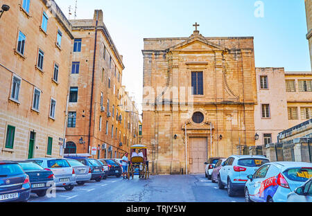 VALLETTA, MALTA - JUNE 19, 2018: The St Mary Magdalene church faces North street, occupied with parked cars, on June 19 in Valletta. Stock Photo
