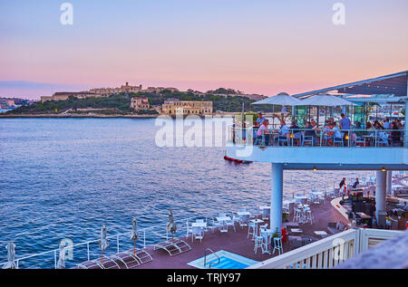 SLIEMA, MALTA - JUNE 19, 2018: The crowded open air terrace of the coastal restaurant on Tigne Point peninsula with a view on Valletta Northern Harbor