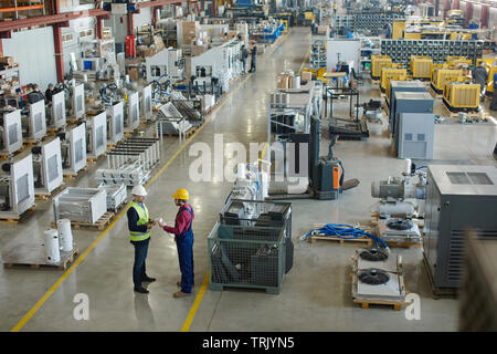 Factory warehouse overview with lined up product, and two colleagues talking in the front Stock Photo