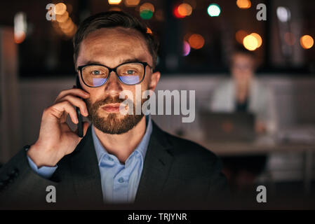 Close up portrait of mid-age businessman using phone, wearing glasses late night at work Stock Photo