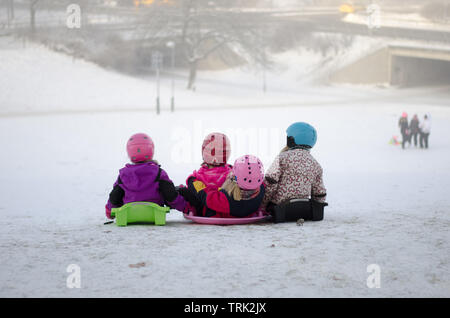 A group of four kids sledding down the hill on a snowy day Stock Photo