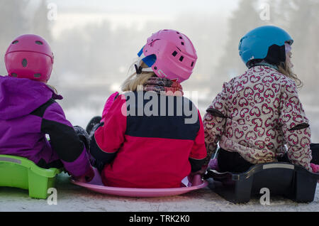 A group of four kids sledding down the hill on a snowy day Stock Photo