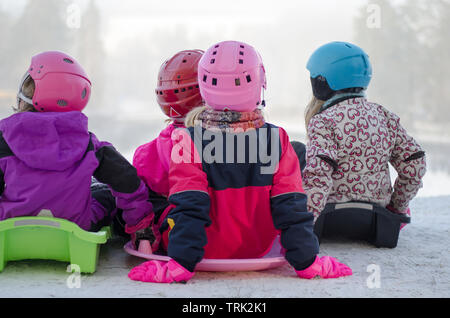 A group of four kids sledding down the hill on a snowy day Stock Photo
