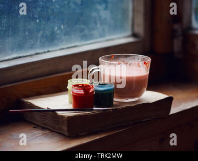 still life from a book, Cup and paints on an old wooden windowsill Stock Photo