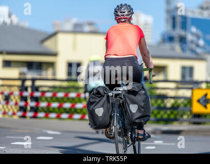 A gorgeous woman cyclist in sportswear and helmet crosses the crossroad on a bicycle, preferring an active way of relaxation, helping her to keep hers Stock Photo