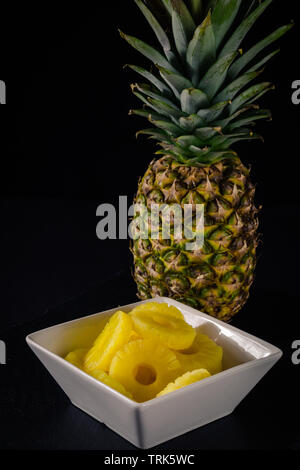 Pineapple on black background. With round ripe pieces of pineapple in a white bowl. Stock Photo