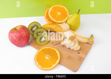 Sliced tropical fruits: kiwi, orange, banana on light wooden board. Stock Photo
