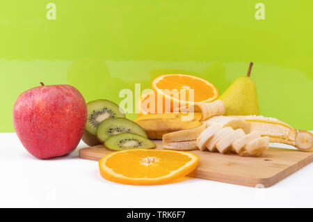 Sliced tropical fruits: kiwi, orange, banana on light wooden board. Stock Photo
