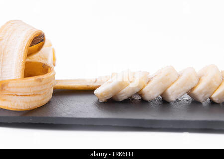 Sliced peeled banana, knife, chopping board. On white background Stock Photo