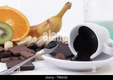 Close up of melted dark chocolate with a creamy texture, a banana and orange behind. White background Stock Photo