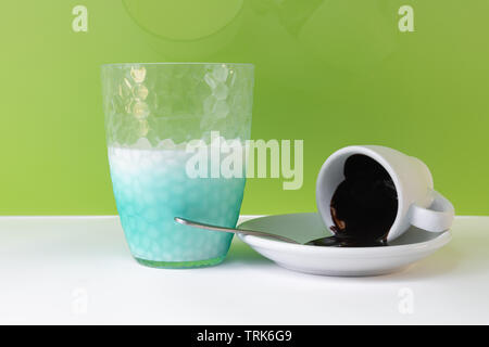 Dark chocolate spilled from coffee cup and a half glass of milk isolated, on green background close up Stock Photo