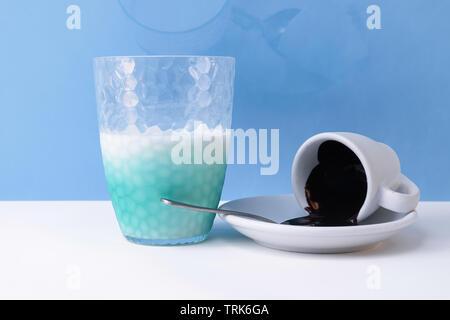 Dark chocolate spilled from coffee cup and a half glass of milk isolated, on blue sky background close up Stock Photo