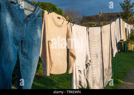 Side view of domestic laundry of wet clothes and towels, pegged and hanging out to dry on a washing line in the warm afternoon sunshine. England, UK. Stock Photo