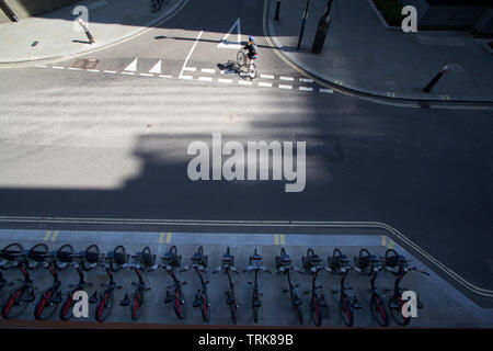 Row of Santander rental hire bike in shadow with passing cyclist Stock Photo