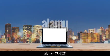Computer laptop blank white screen on wooden desk with blurred Osaka city view at night in Japan. Laptop Computer Background Stock Photo