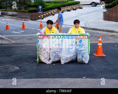 Seoul, South Korea - June 3, 2017: Two young korean men sitting near waste sorting containers with colored inscriptions for plastic, glass bottles. Stock Photo