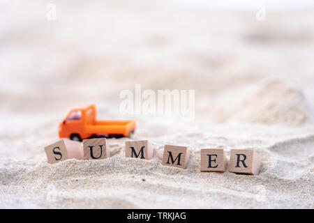 Summer word written on wooden block put on the sand beach. Sea view during daytime with blue sky background. Summer season concept. Stock Photo