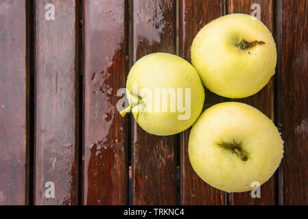 Three golden green apples of Beliy Naliv variety on brown wet natural old wooden table surface. Ripe fruits are covered by raindrops. Flat lay with co Stock Photo