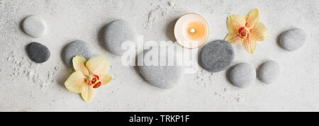 Spa concept on white stone background, tropical orchid flowers, candle and zen like grey stones, top view, banner. Stock Photo