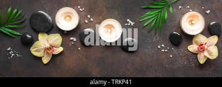 Spa concept on dark background, palm leaves, candles and zen like black stones, top view, banner. Spa composition. Stock Photo