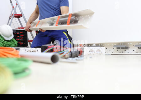 electrician at work with the plastic pipe in his hand to pass the electric cables to the sockets, electric circuits, electrical wiring Stock Photo