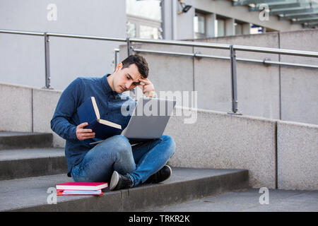 Stressed student preparing for an exam in campus area sitting on university stairs. Student man with laptop, sitting on university stairs. Technology, Stock Photo