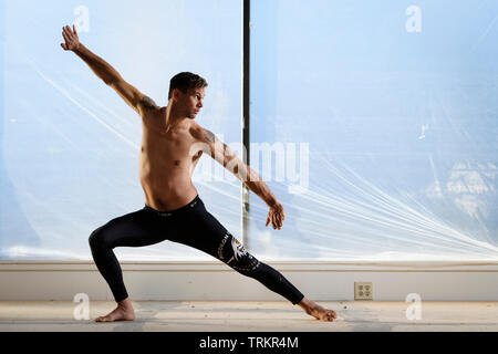 Man practicing Budokon Yoga with no shirt on in a warehouse. Stock Photo