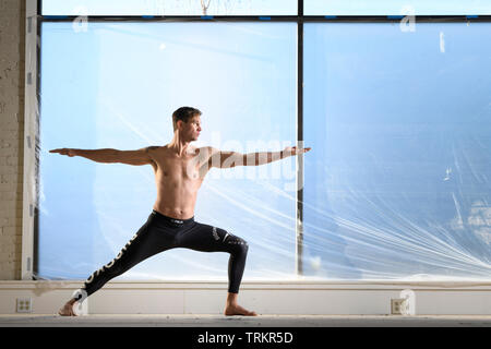 Man practicing Budokon Yoga with no shirt on in a warehouse. Stock Photo