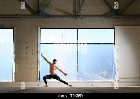 Man practicing Budokon Yoga with no shirt on in a warehouse. Stock Photo