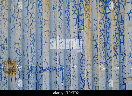 Abstract view of old vertically corrugated metal wall, with corrosion, rust and cracked blue paint. Stock Photo